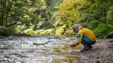 Een wandelaar hurkt bij de rivier de Alb op de Albsteig Schwarzwald en schept water in zijn handen