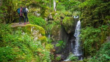 Twee wandelaars staan op een rots boven de Höllbachwatervallen