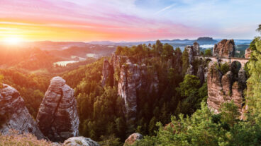 Een uitzicht op de Basteibrug vanaf het Ferdinand-uitkijkpunt met een zonsopgang boven het Nationaal Park Sächsische Zwitserland