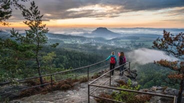 Twee wandelaars bekijken de zonsondergang vanaf een uitzichtpunt op de Papststein