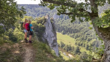 Twee wandelaars staan op de top van de Stiegelesfelsen en kijken het Donau-dal in met de rivier beneden
