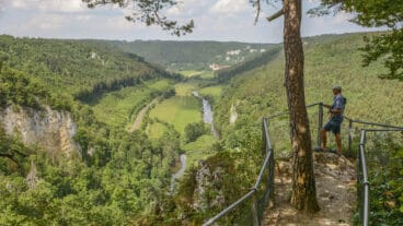 Een wandelaar staat op de top van de Knopfmacherfelsen en kijkt het Donau-dal in naar de rivier beneden