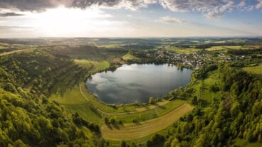 Een luchtbeeld van het vulkanische kratermeer Schalkenmehrener Maar met het dorp Schalkenmehren ernaast