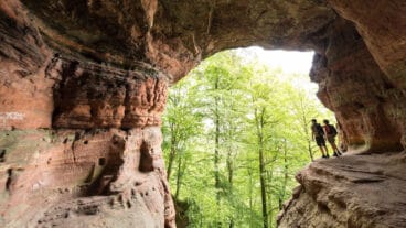 Twee wandelaars staan bij de ingang van de Genovevahöhle