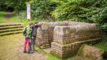 Twee wandelaars kijken in de Romeinse ruïnes van de bronopvanginstallatie Grüner Pütz